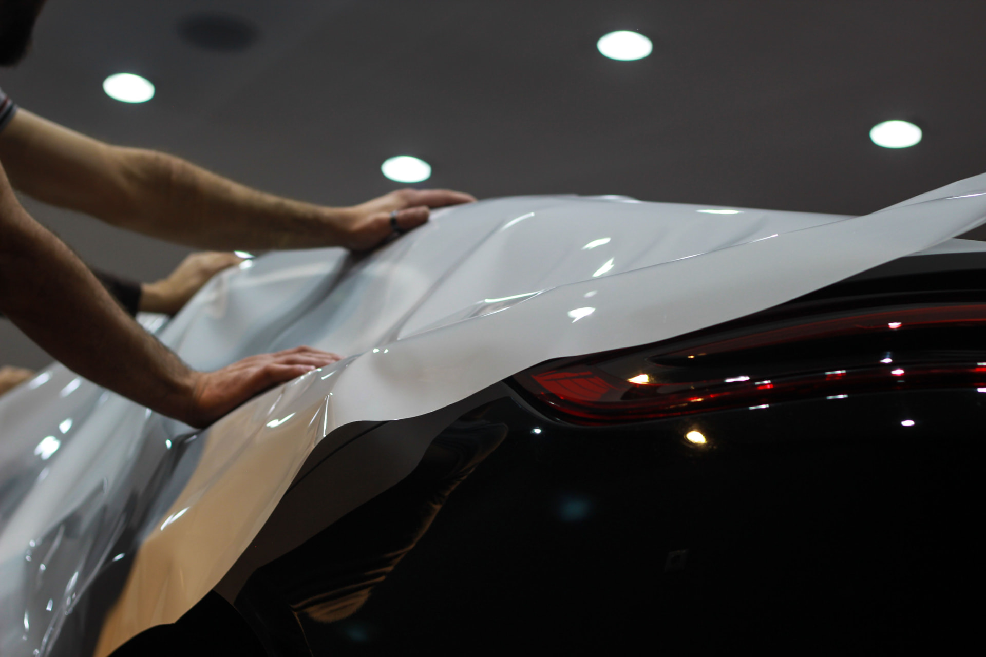 Car wrapping service - hands smoothing glossy film over a car's rear panel