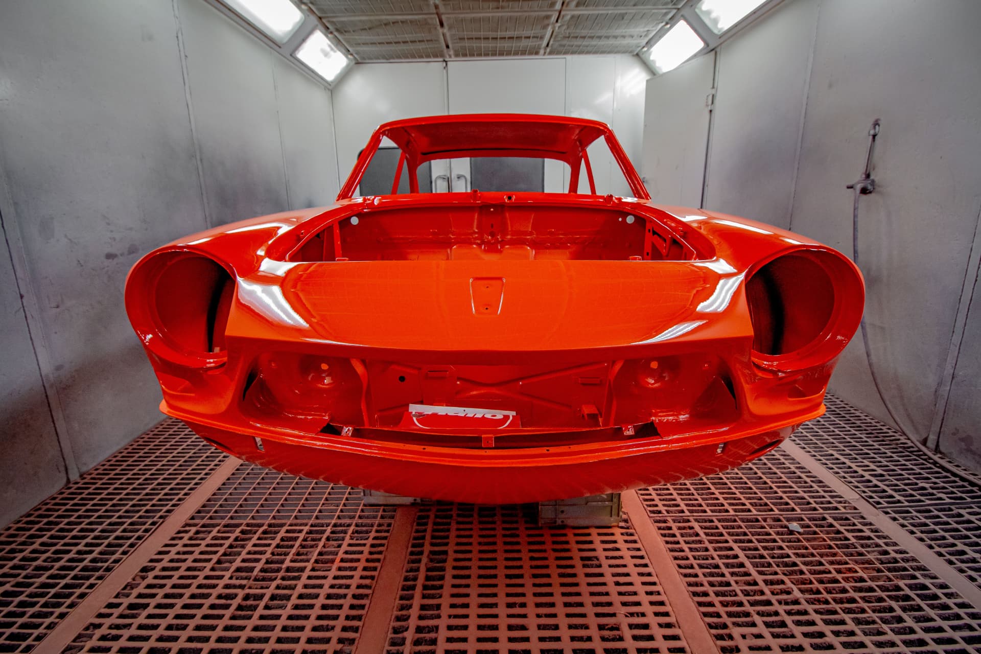Bodywork restoration service - classic car body shell freshly painted red in a paint booth