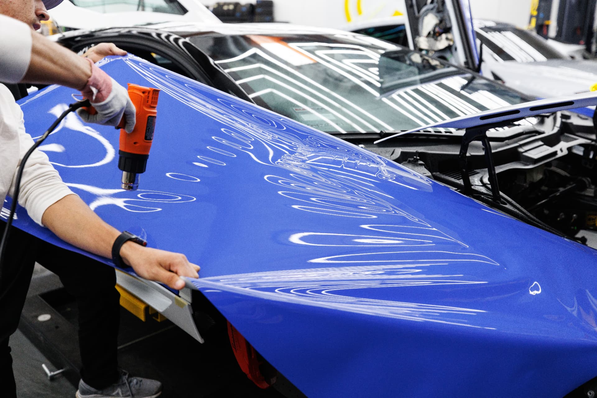Paint protection film installation - technician applying film to a car hood